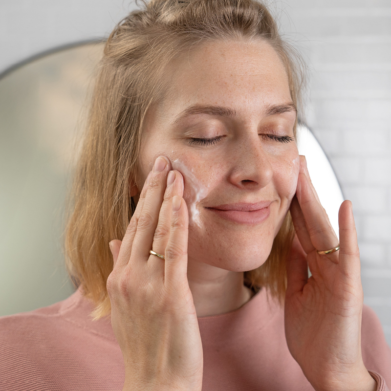 Vrouw brengt glimlachend crème aan op de wangen