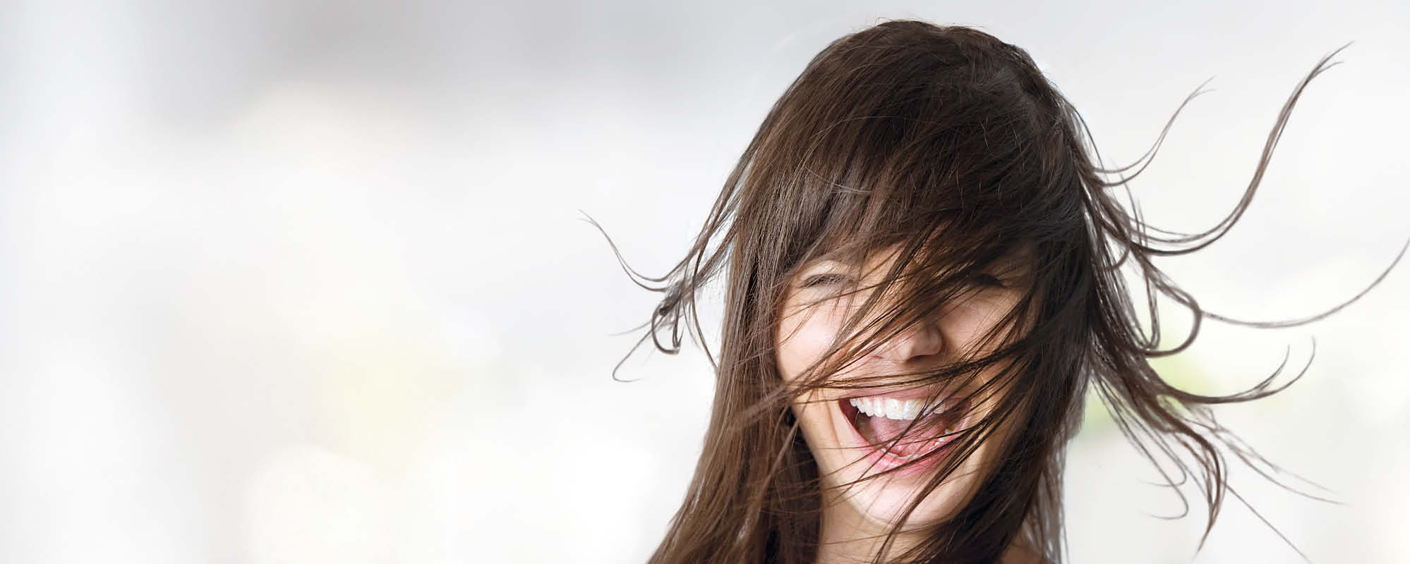 Brunette woman's healthy hair blows across her face