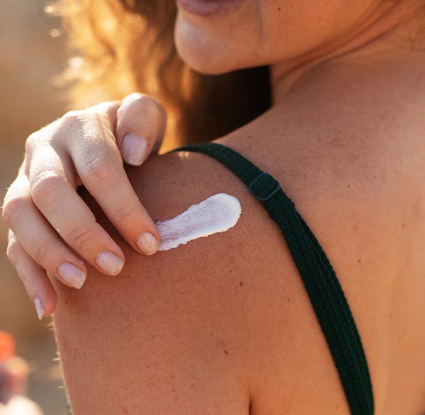 De vrouw smeert zonnebrandcrème op haar schouder