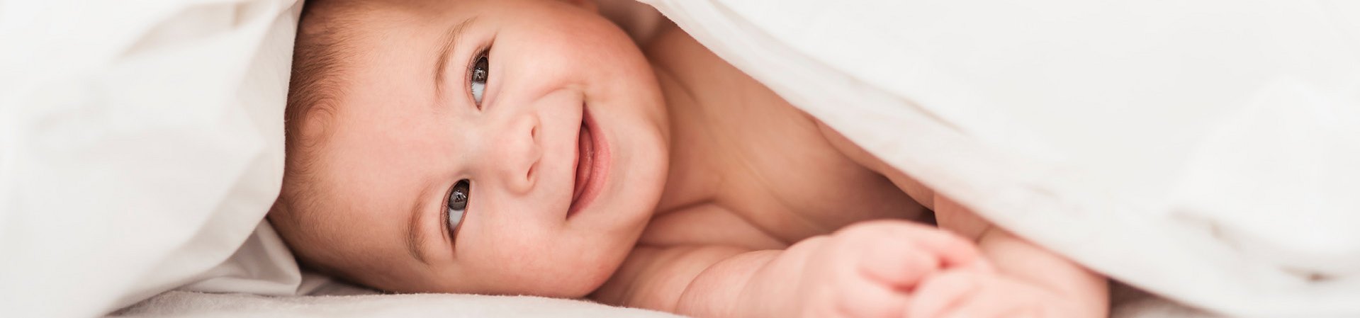 La pelle del bambino richiede una cura della pelle particolarmente compatibile Bambino sorridente sotto una coperta bianca
