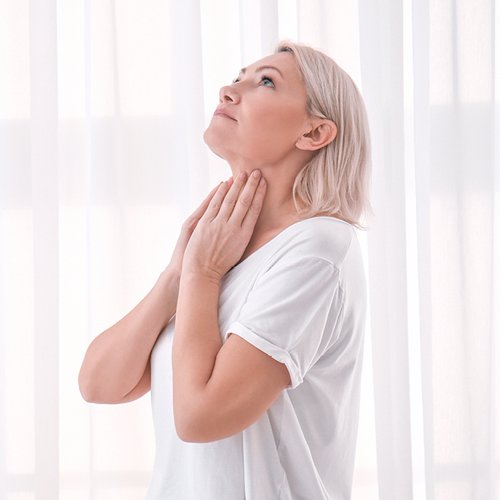 Blonde vrouw raakt haar schildklier aan de hals aan.