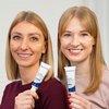 Two women hold the RosaMin Tinted Day Creams in light and medium shades next to their faces.