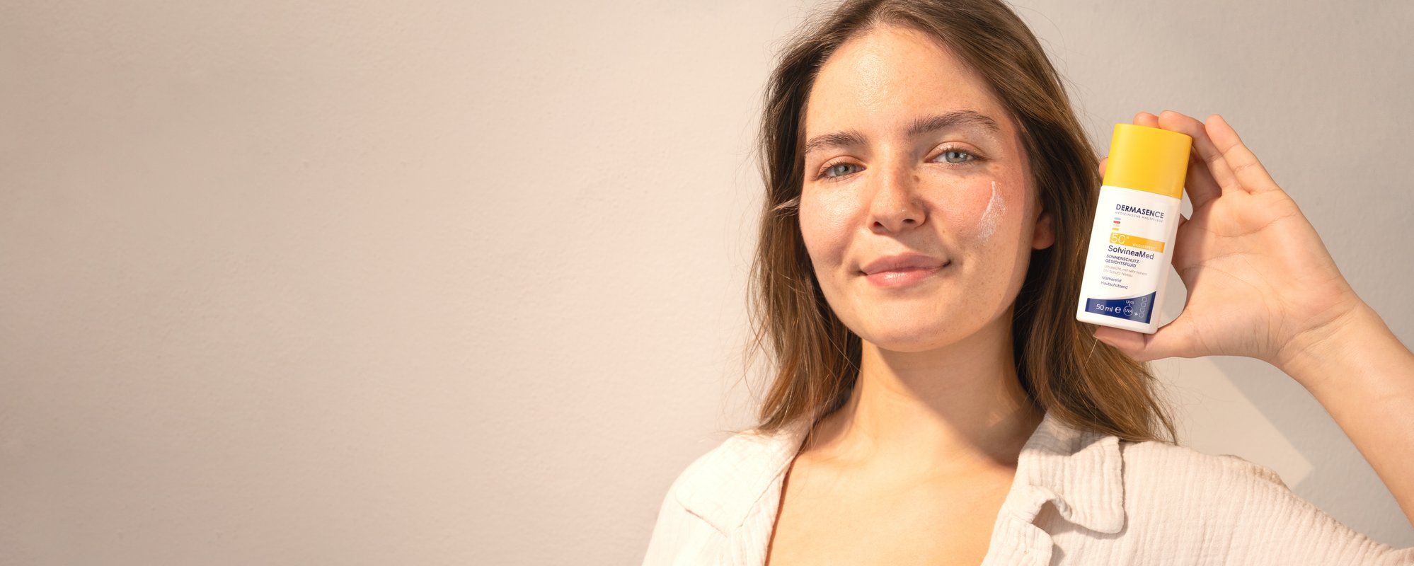A brunette woman smiles as she holds a product next to her face