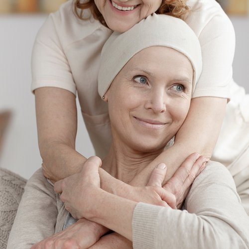 [Translate to Niederländisch:] Lächelnde Krebspatientin wird von Frau umarmt