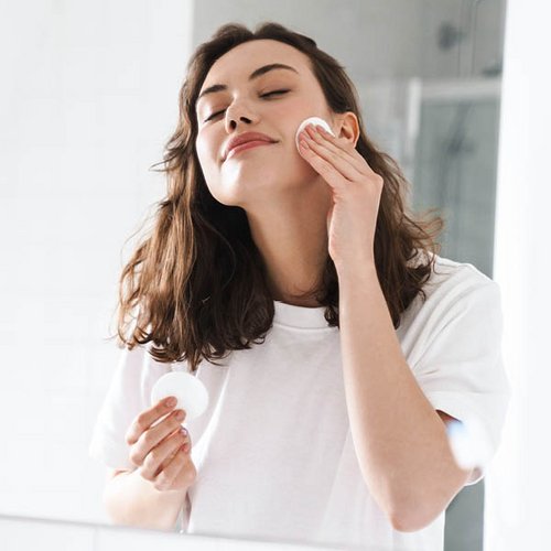 Een bruinharige vrouw reinigt haar gezicht met een wattepad