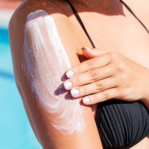 Een vrouw aan het zwembad smeert haar bovenarm in met SPF