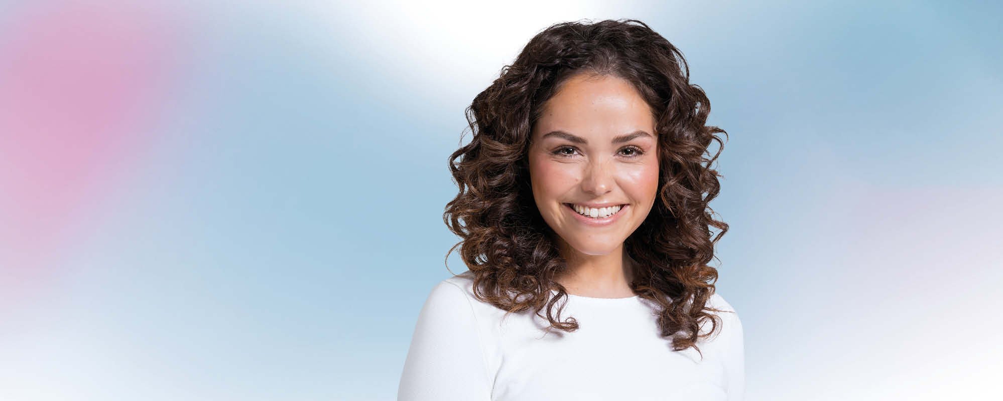 Glimlachende jonge vrouw met bruine krullen tegen een blauwe en roze achtergrond