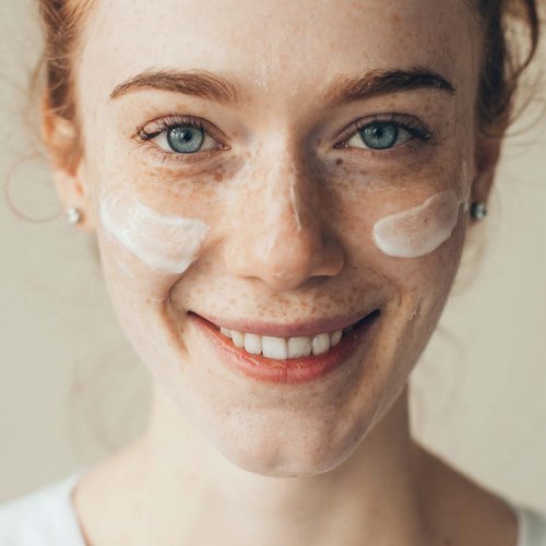 Roodharige vrouw met verzorgingscrème op de wangen