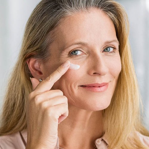 Blonde vrouw smeert crème onder haar oog