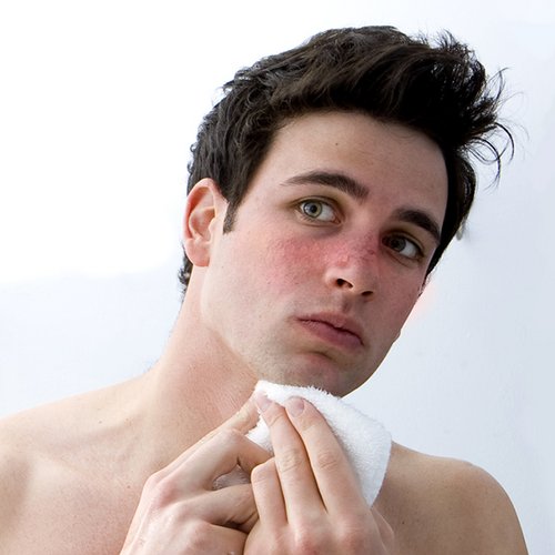 Een jonge man kijkt in de spiegel naar zijn huid.