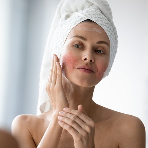 [Translate to Niederländisch:] Frau mit Hautrötungen cremet ihre Wange ein