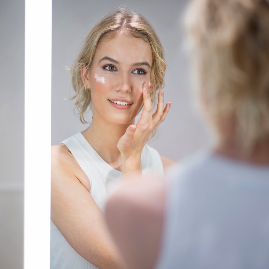 Woman applies a face cream with UV protection in front of the mirror