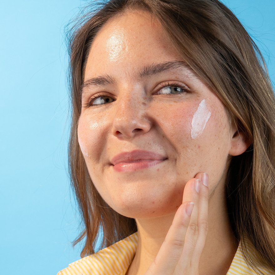 Visage d’une femme châtain, souriante, avec de la crème sur la joue